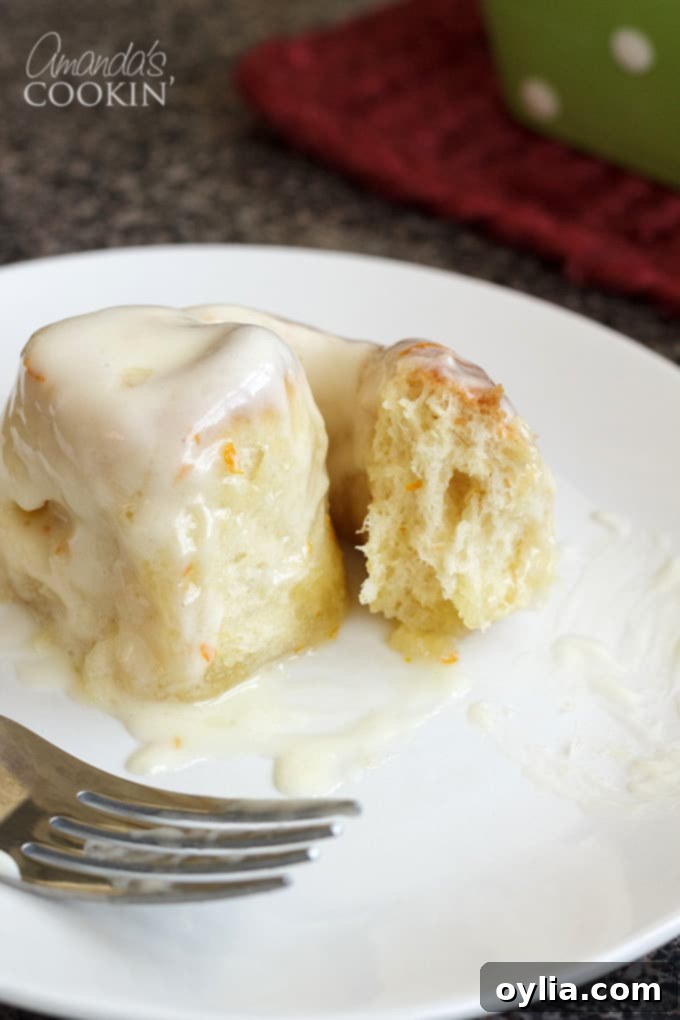 A single, perfectly frosted homemade orange roll resting on a white plate, showcasing its soft texture and inviting glaze.