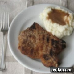 An overhead photo of a grilled breaded pork chop on a white plate with mashed potatoes and gravy and a fork.