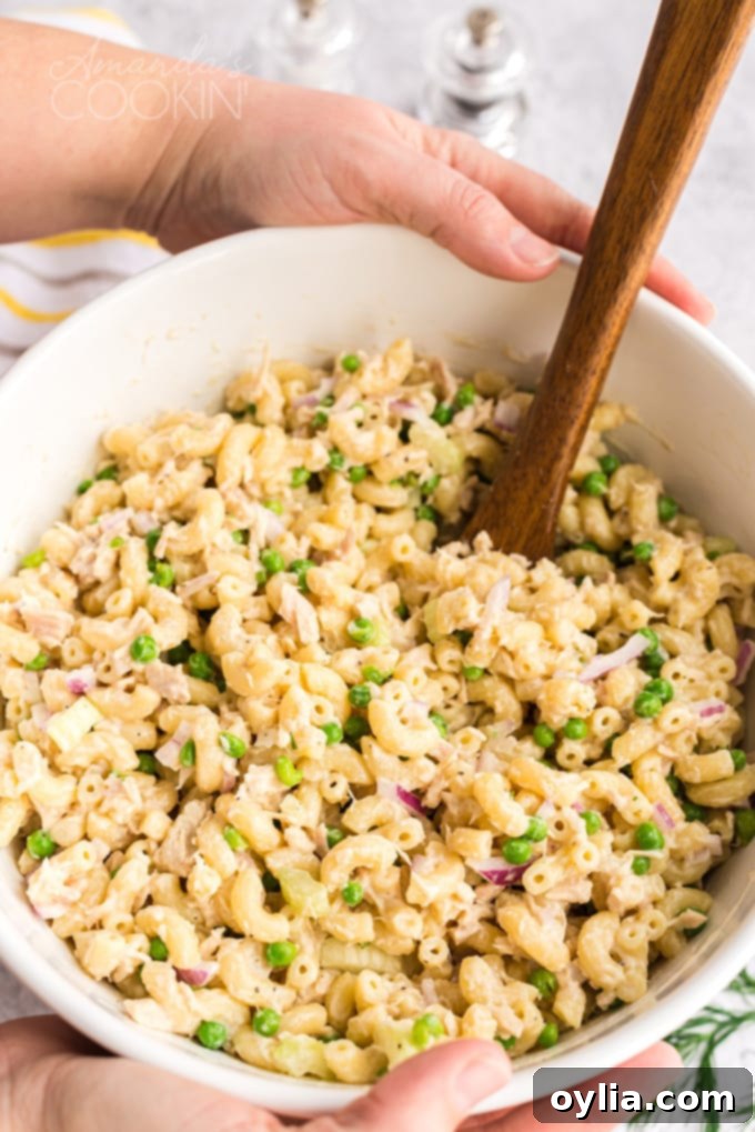 This easy tuna pasta salad recipe is perfect for potlucks and barbecues, or simply a protein-packed and satisfying lunch! Someone holding a large bowl of homemade tuna pasta salad, ready to serve