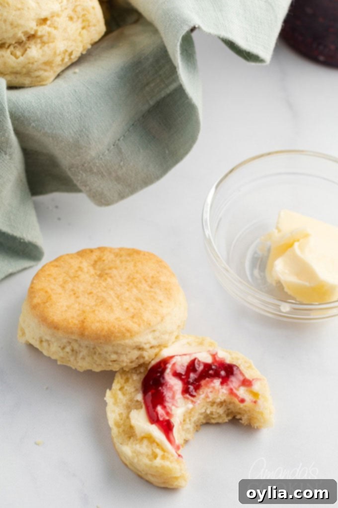 A close-up shot of a golden homemade biscuit, split open and generously topped with vibrant red berry jam