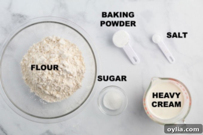 A selection of the five simple ingredients needed for homemade biscuits: flour, baking powder, sugar, salt, and a pitcher of heavy cream