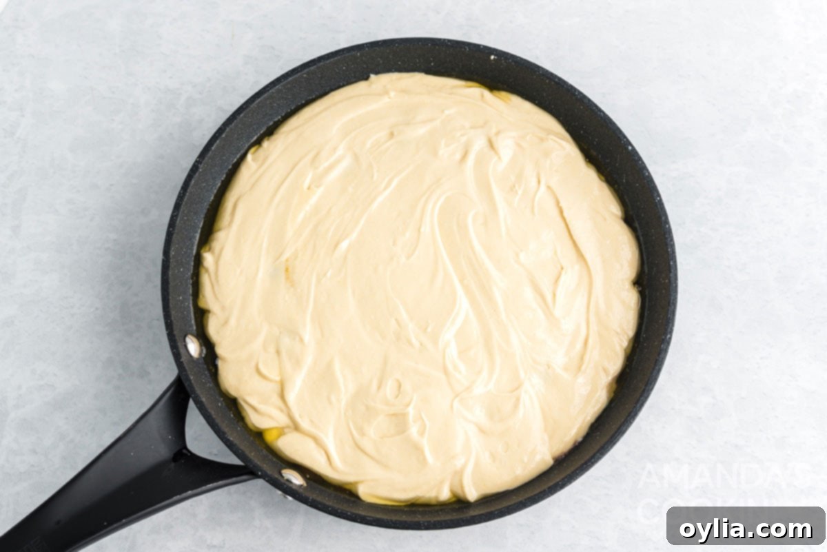 The cake batter evenly spread over the pineapple topping in a cast iron skillet, ready for baking.