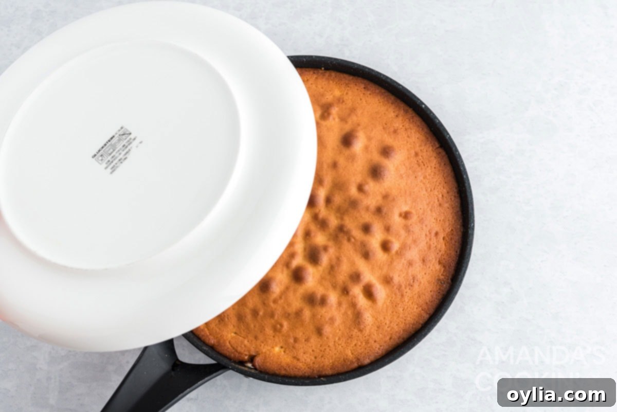 Placing a flat cake plate over the hot cast iron skillet, preparing to invert the pineapple upside down cake.
