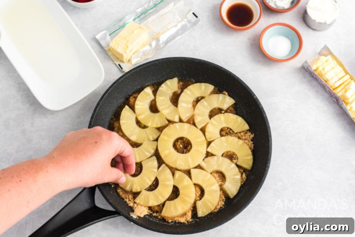 Carefully placing pineapple rings onto the brown sugar layer in the cast iron skillet for the cake topping.