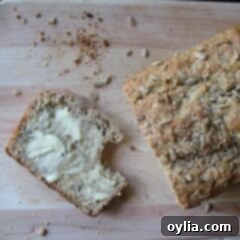 A photo of a loaf of sunflower whole wheat quick bread with a buttered slice to the side all resting on a wooden cutting board.