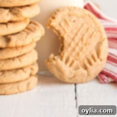 A delicious peanut butter cookie with a bite taken out, stacked with other cookies and a glass of milk.