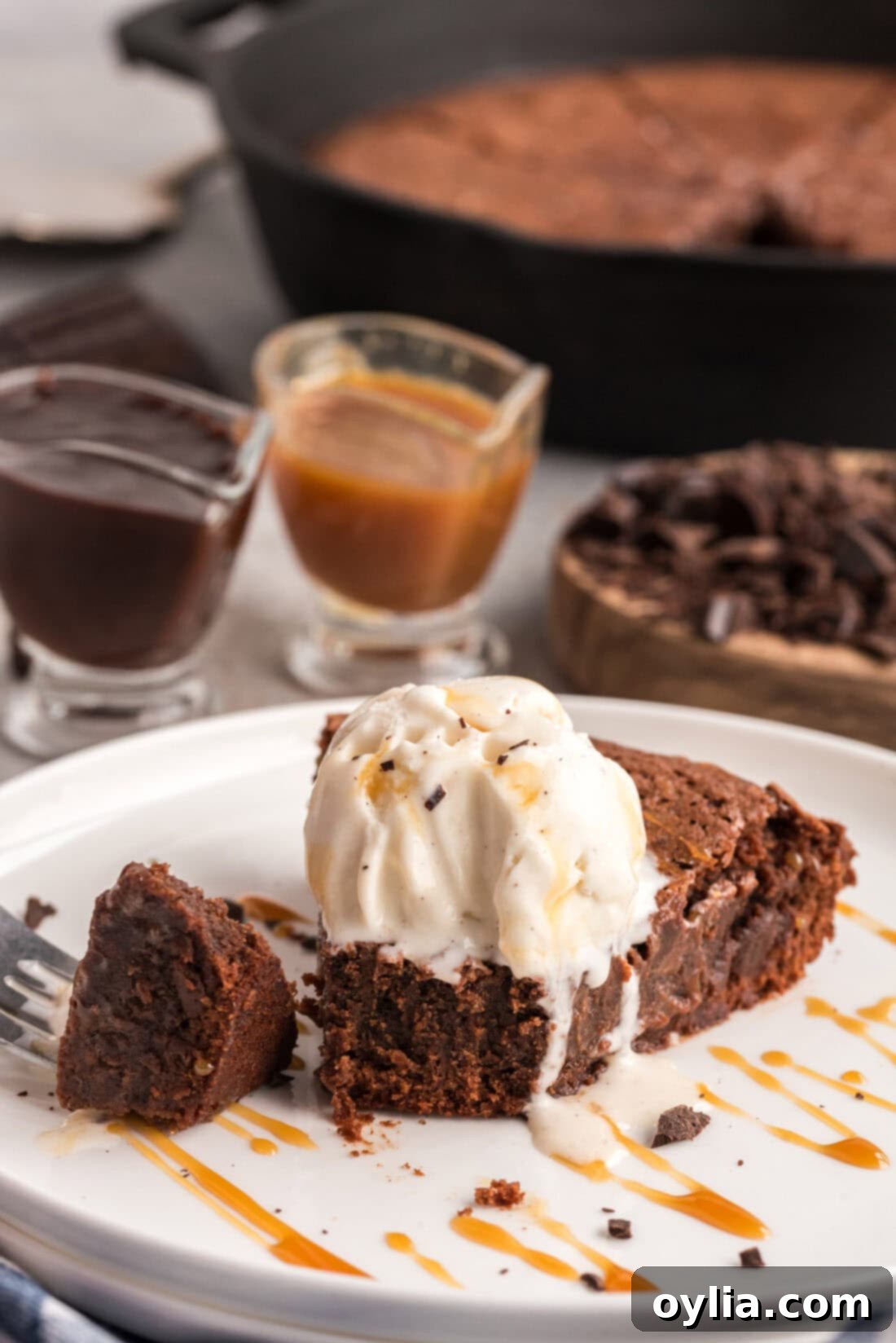 A delectable slice of cast iron skillet brownie on a white plate, generously topped with a scoop of melting vanilla ice cream, showcasing its rich, fudgy texture.