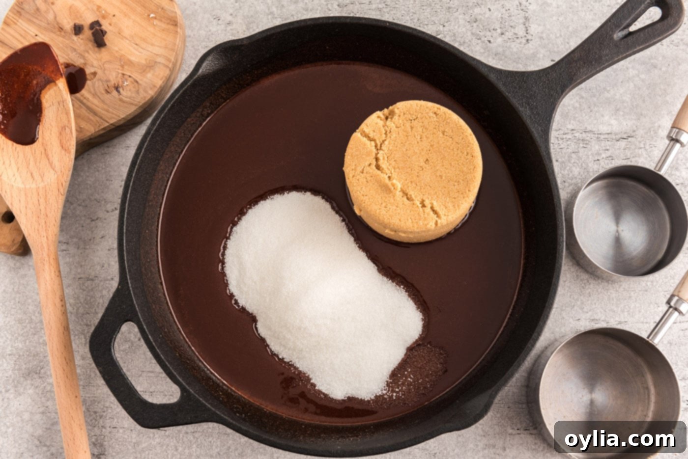 Both light brown sugar and granulated sugar being stirred into the melted chocolate and butter mixture in a cast iron skillet, creating a smooth, glossy base for the brownies.