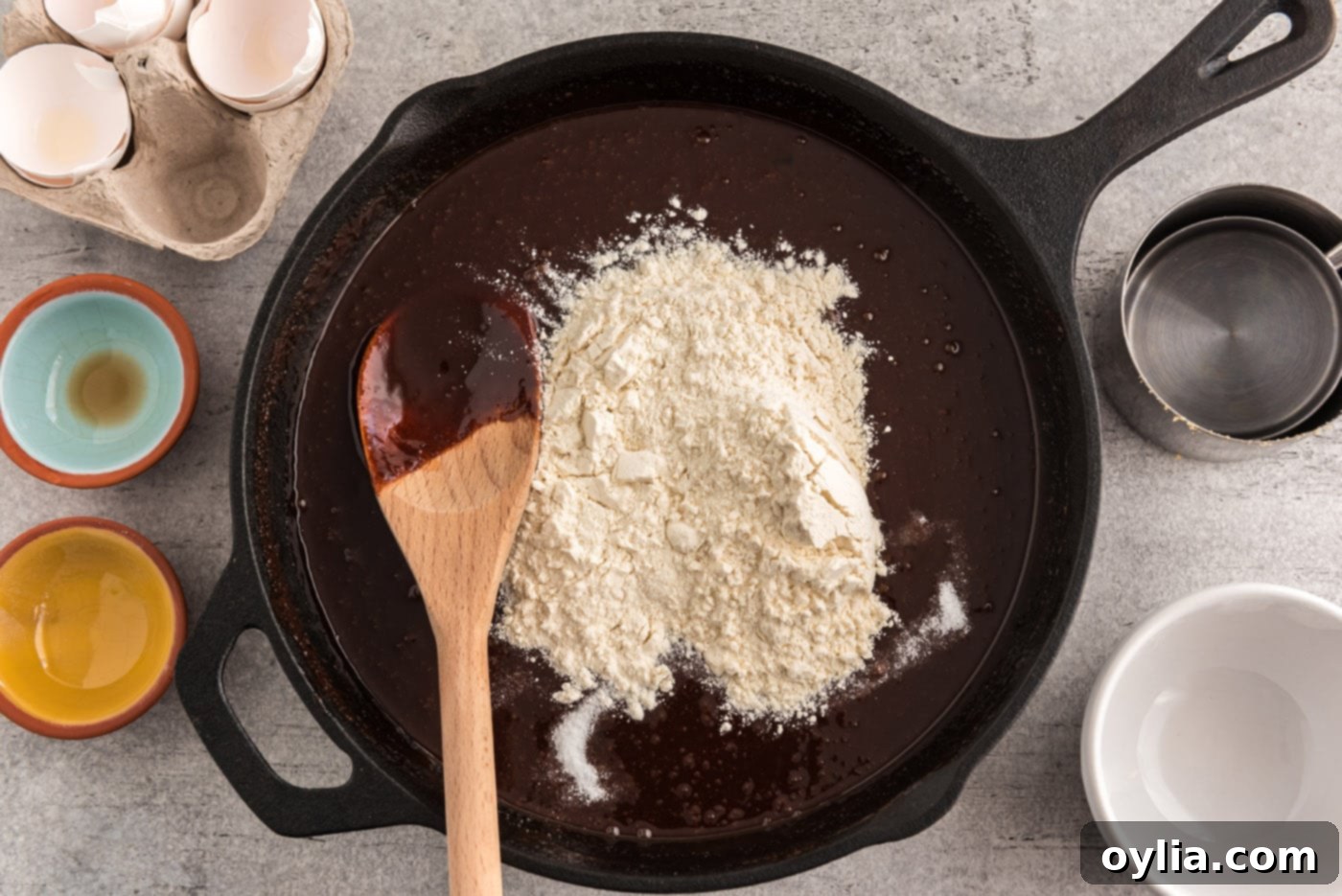 A dusting of all-purpose flour and salt resting on top of the rich, dark chocolate brownie mixture in a cast iron skillet before being gently folded in.
