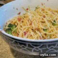 A close up photo of spaghetti with pancetta and broccoli in a bowl.