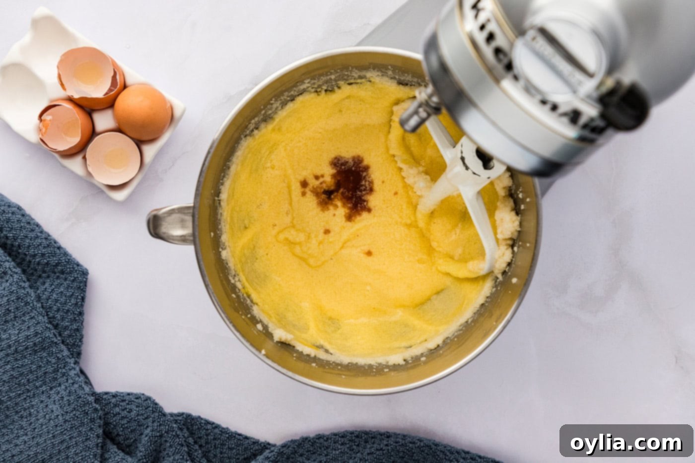 Vanilla extract being added to the creamed butter and sugar mixture in a stand mixer bowl