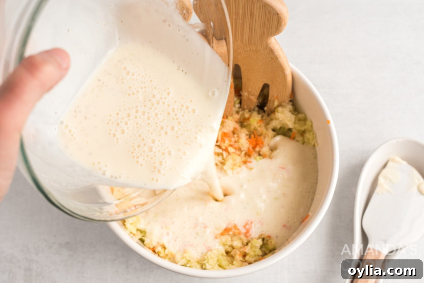 Pouring the creamy dressing over the chopped cabbage, carrots, and onion for coleslaw.