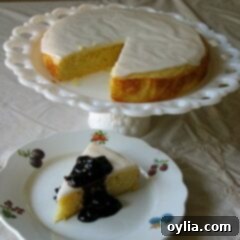 A photo of a lemon cornmeal cake missing a slice on a white cake stand next to a slice of cake on a white plate topped with blueberry sauce.