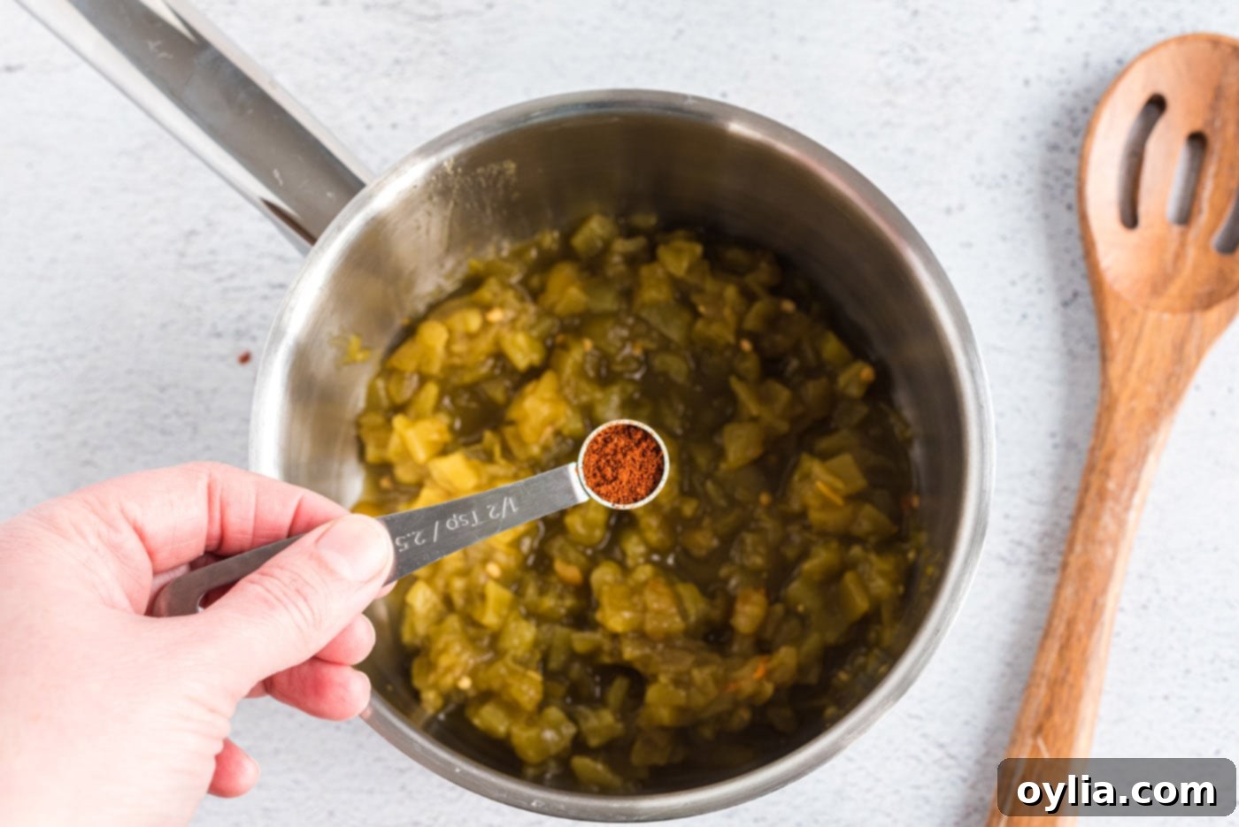 Sprinkling chili powder into a saucepan filled with diced green chiles, heating to release their aromatic flavors for the sauce.