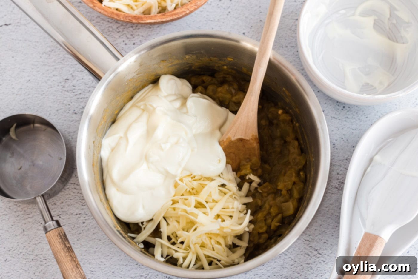 Stirring sour cream into the green chile and flour mixture in a saucepan to create a smooth, creamy sauce base.