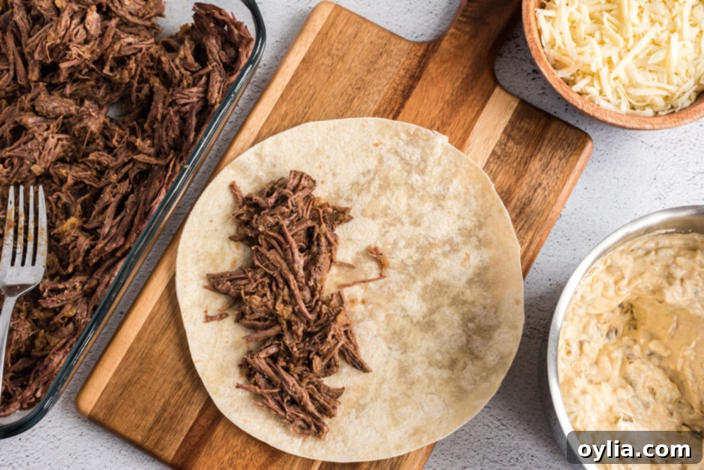 A soft flour tortilla generously filled with seasoned shredded beef, ready to be topped with sauce and rolled.