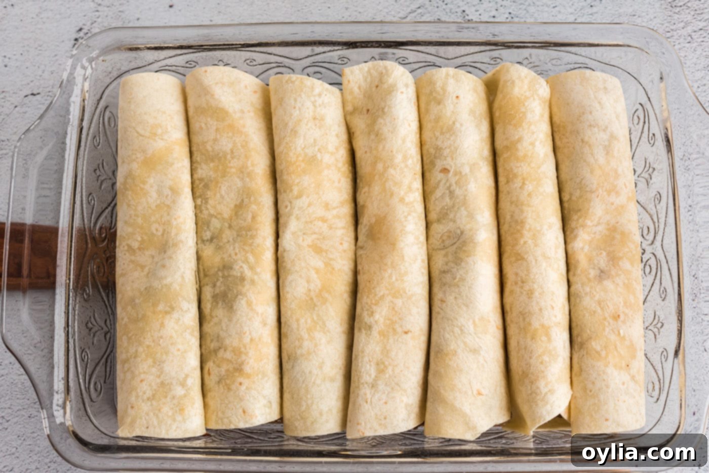 A baking dish neatly filled with rolled beef enchiladas, arranged seam-side down, ready for the oven.