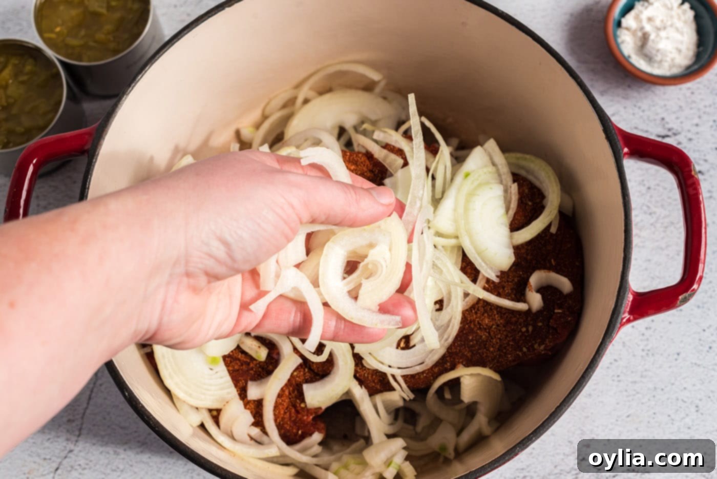 Thinly sliced white onions being artfully arranged over a seasoned chuck roast in a roasting pan, ready for slow cooking.