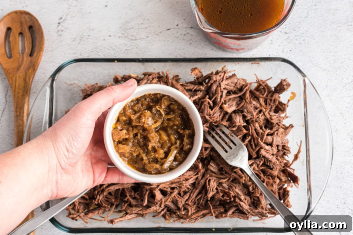 Adding savory sautéed onions to a bowl of freshly shredded beef, blending the flavors for the enchilada filling.