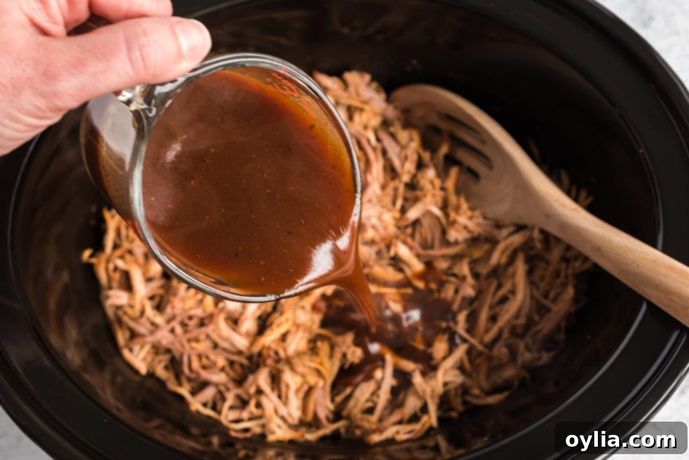 Easy Slow Cooker Pulled Pork 12 Pouring thickened sauce over shredded pulled pork