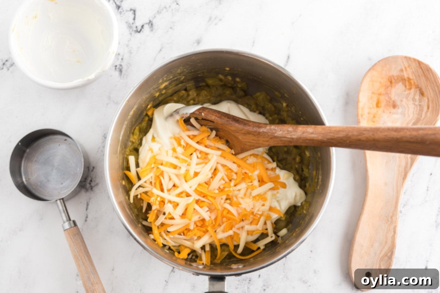 Sour cream and shredded cheese added to a pan with green chiles, creating a creamy sauce