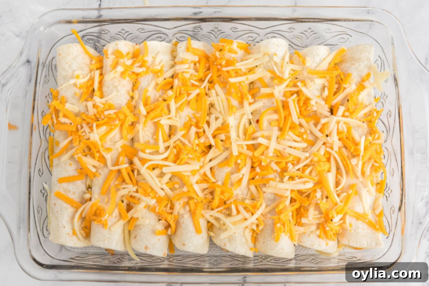 Enchiladas topped generously with shredded cheese, ready for final baking