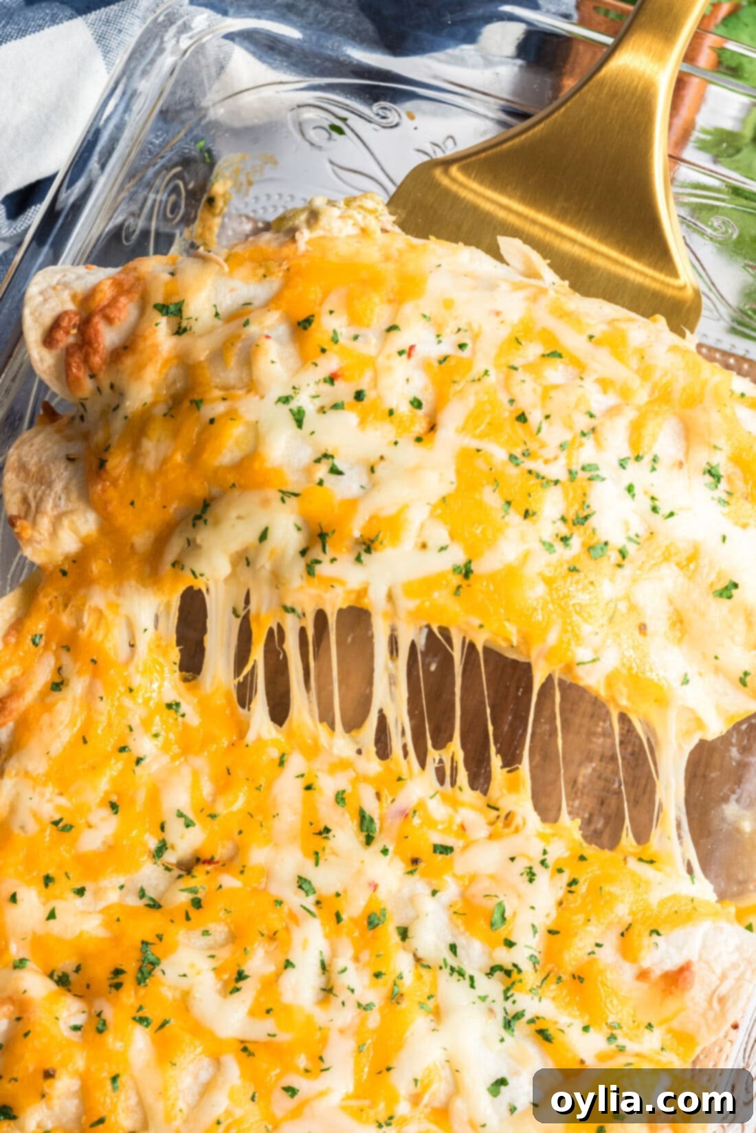 Spatula lifting two perfectly baked Shredded Chicken and Green Chile Enchiladas from the pan