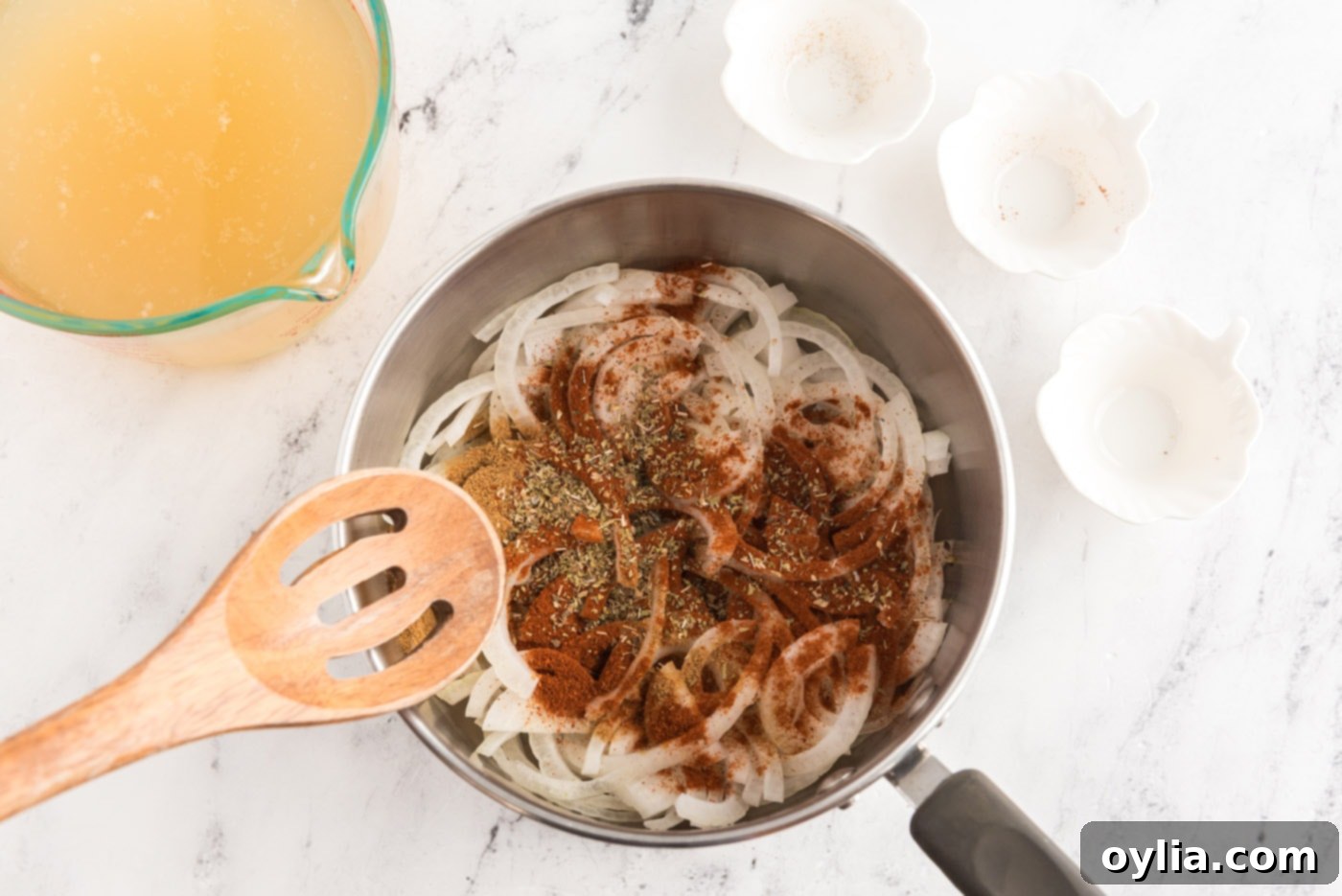 Sliced onion with chicken broth, spices, and seasonings simmering in a saucepan