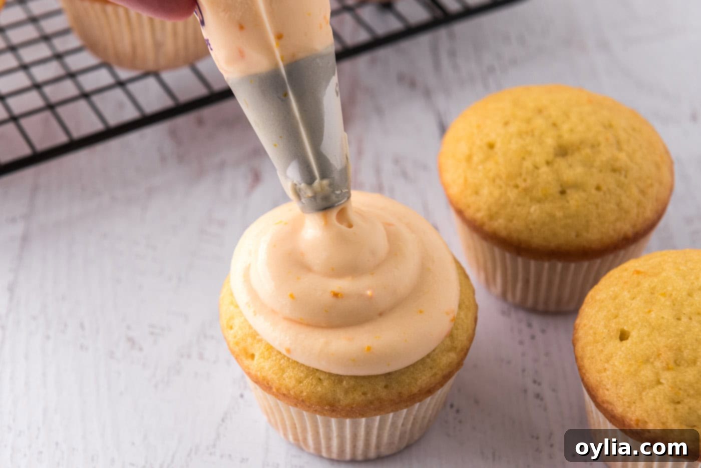 Piping orange creamsicle frosting onto cupcakes with a pastry bag, creating a beautiful swirl design.