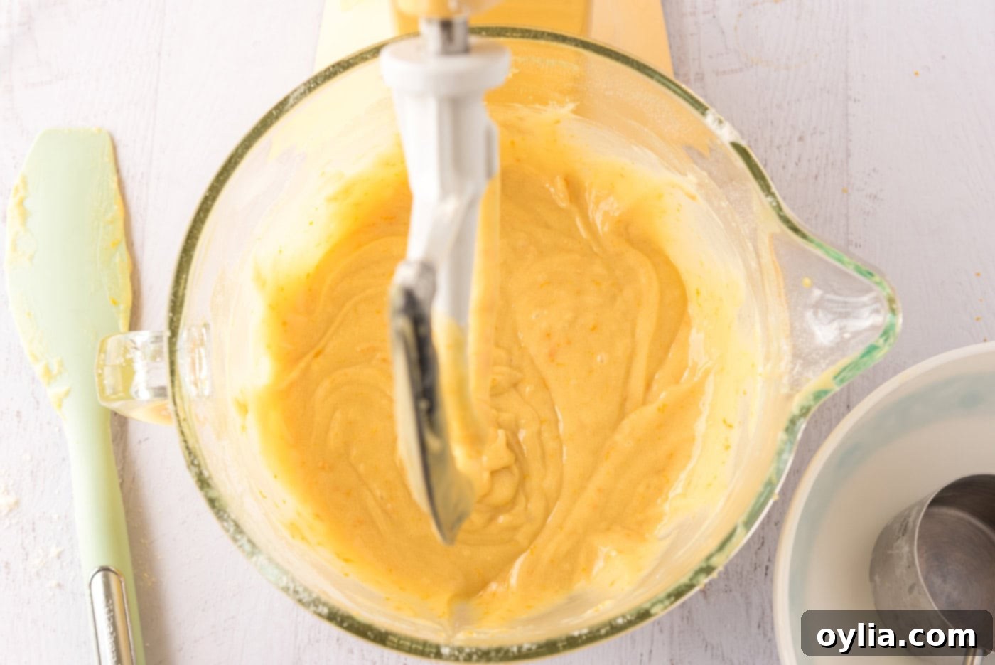 Close-up of orange cupcake batter in a stand mixer bowl, showing its smooth and vibrant consistency.