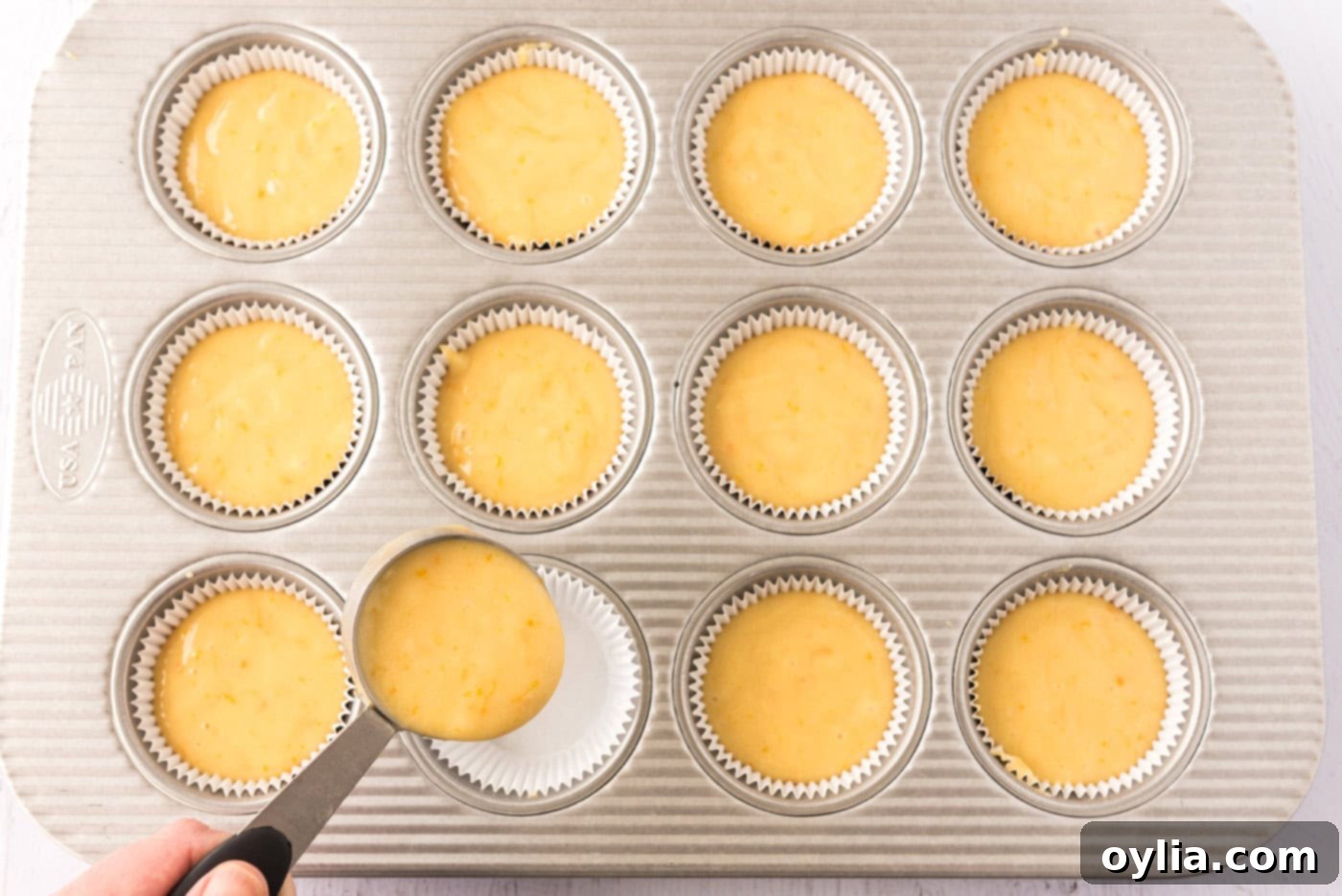 Spoonfuls of orange cupcake batter being carefully placed into a cupcake pan lined with paper liners.