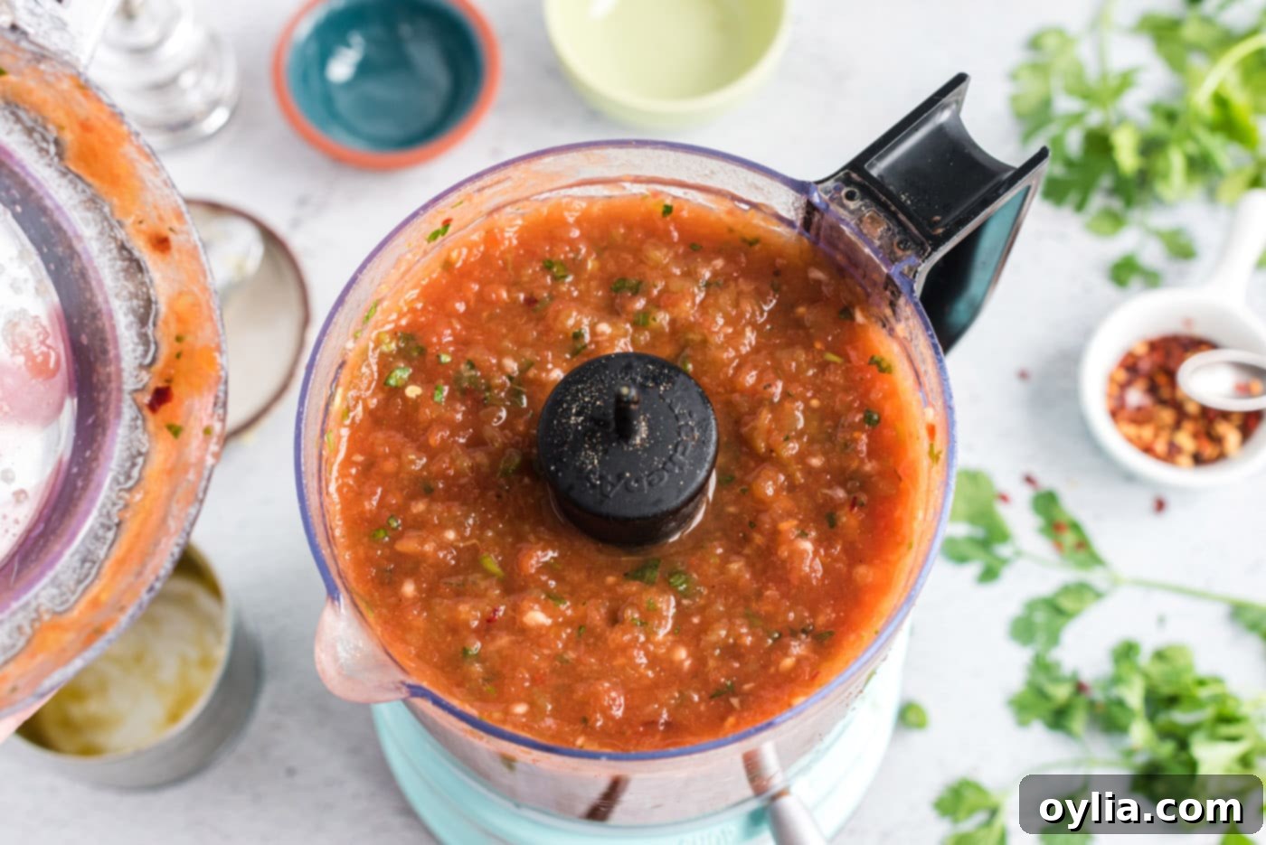 Freshly blended restaurant style salsa inside a food processor bowl, showing a smooth yet slightly chunky texture.