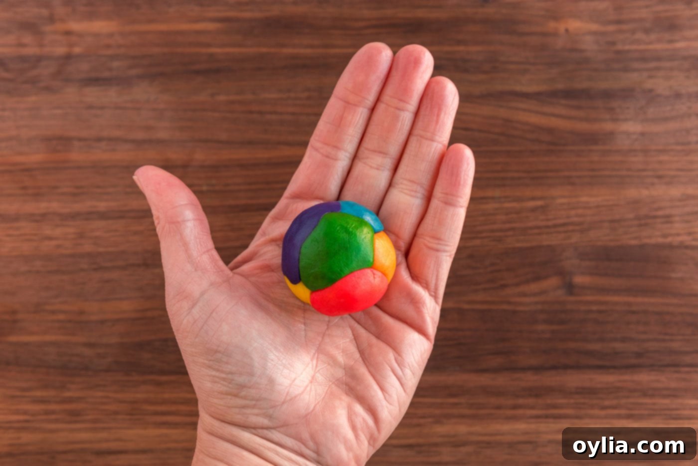 Hand holding a ball of colorful cookie dough with rainbow hues.