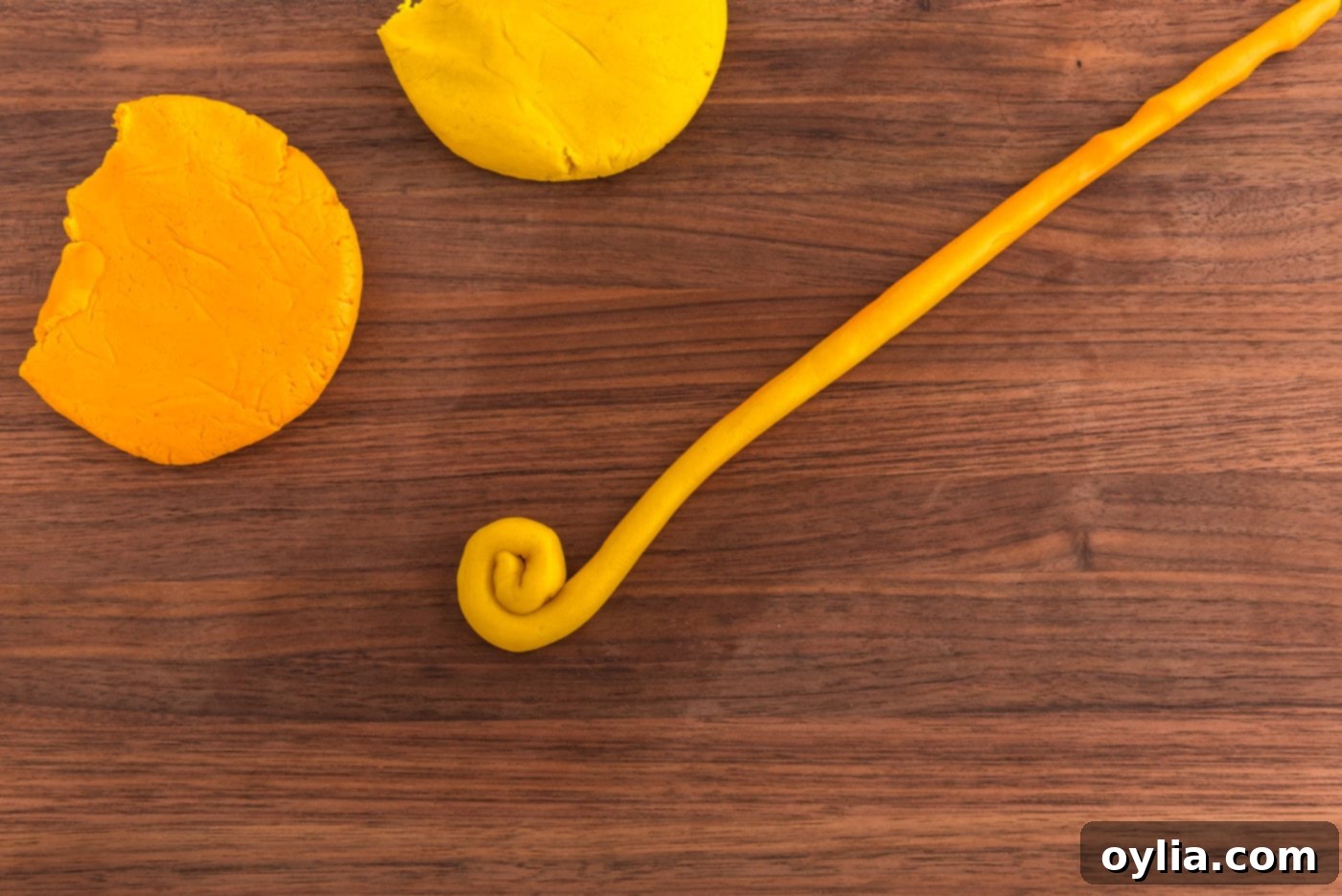 Rolling two shades of yellow cookie dough into a coil to form a gold coin.