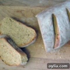 An overhead photo of a sliced loaf of rustic rosemary garlic bread resting on a wooden cutting board.