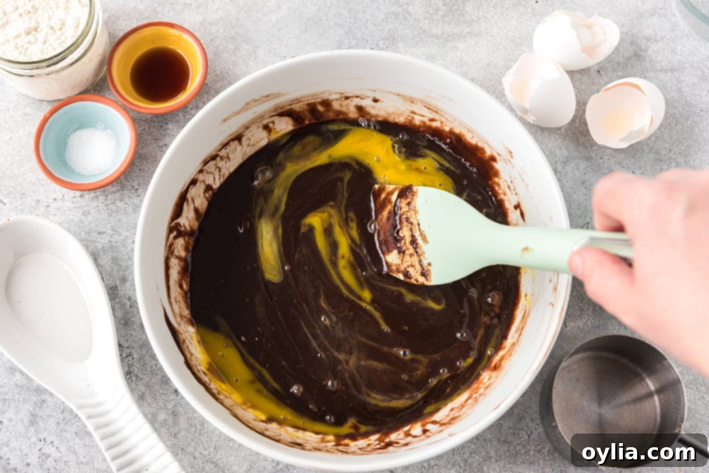 rubber spatula stirring egg into brownie batter in a bowl