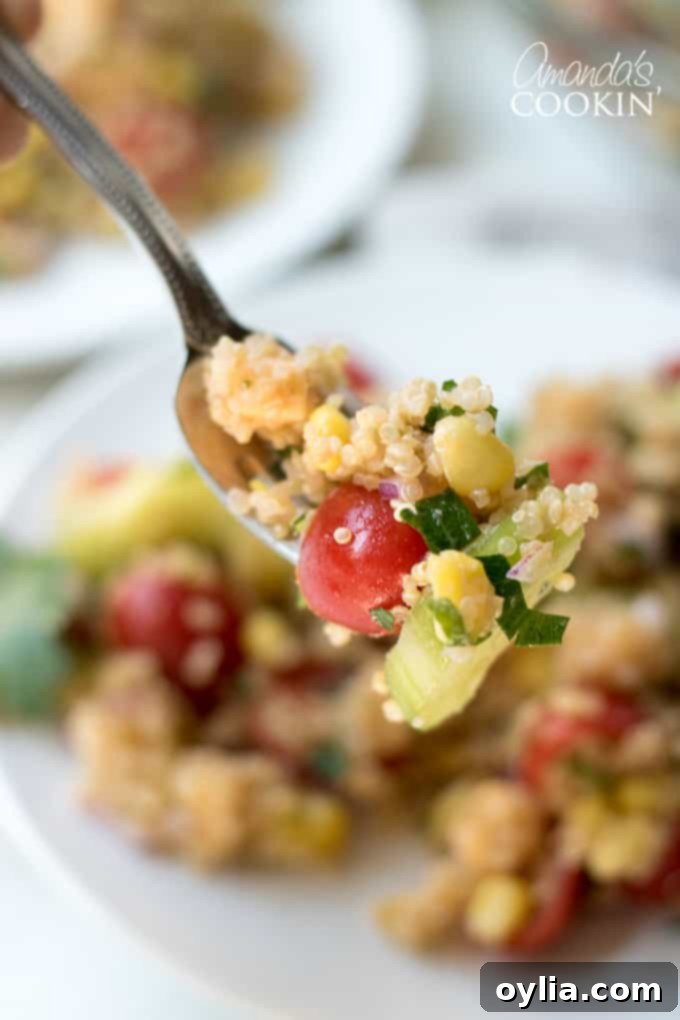 A close-up of a spoon scooping a portion of the refreshing summer vegetable quinoa salad, showing off its textures and ingredients.