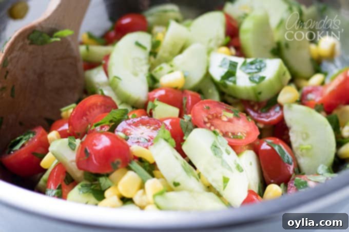 A large bowl filled with vibrant summer vegetables and cheese, lightly tossed together.