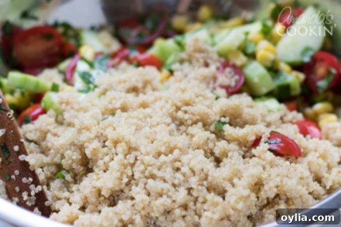 Adding the perfectly cooked and cooled quinoa to the colorful mixture of summer vegetables.