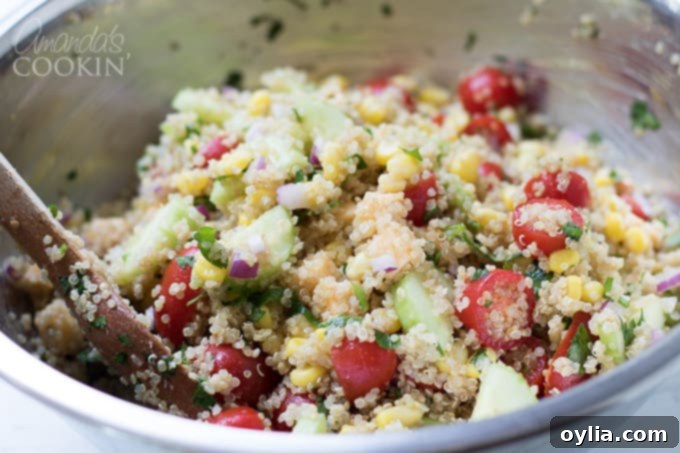 The summer vegetable quinoa salad is thoroughly tossed, ensuring all ingredients are well-mixed.