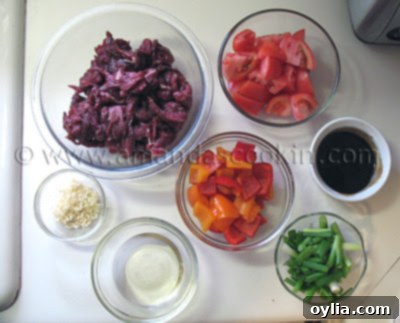 Bowls filled with all the prepped ingredients for beef stir fry: sliced beef, bell peppers, tomatoes, scallions, garlic, ginger, and sauce components