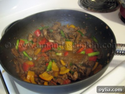 A photo of beef stir fry with tomatoes and peppers being cooked in a wok, showing vibrant colors and steam.