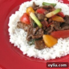 A photo of beef stir fry with tomatoes and peppers over rice.