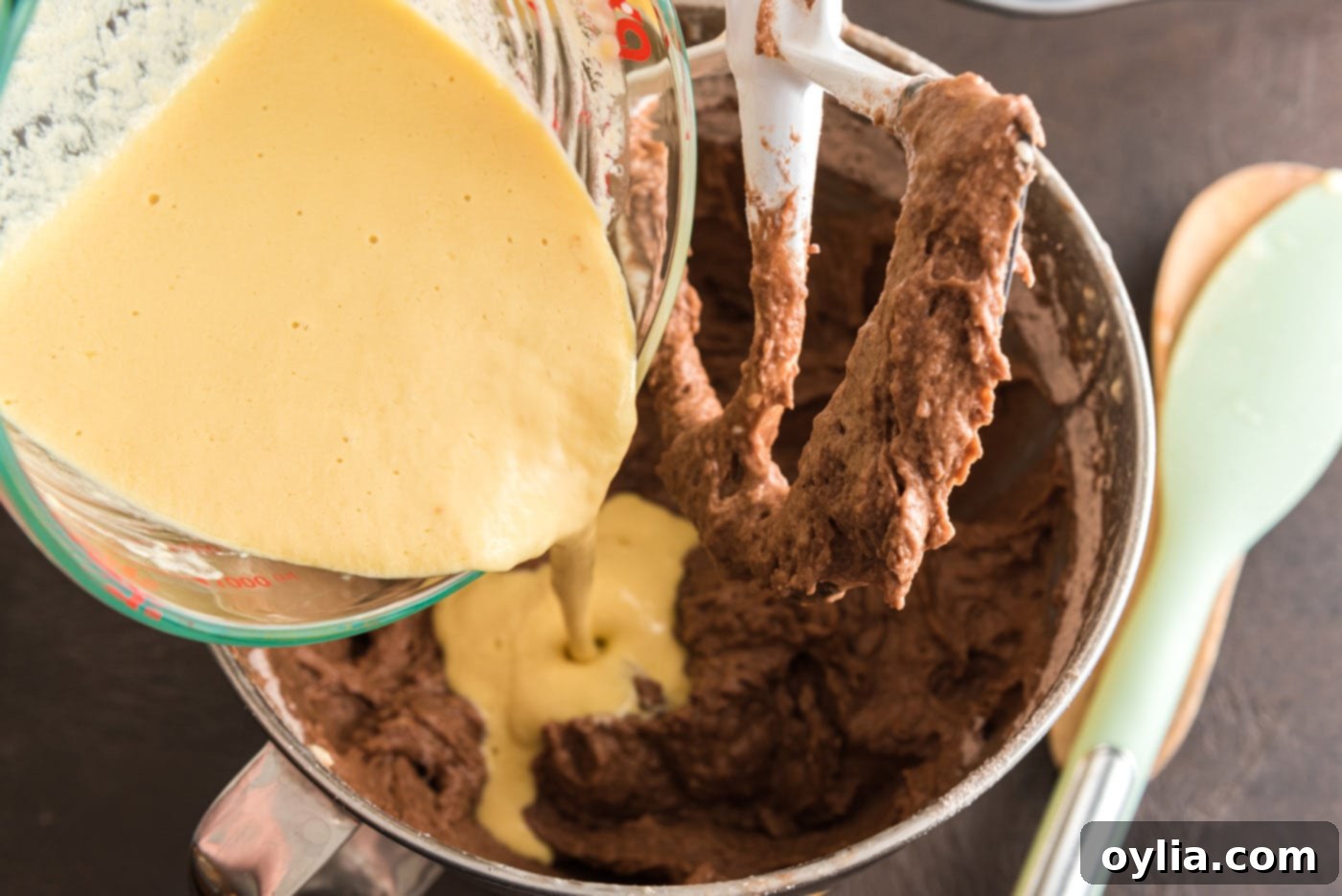 The whisked egg, sour cream, and vanilla mixture is poured into the chocolate cake batter in a stand mixer, ready for final mixing.