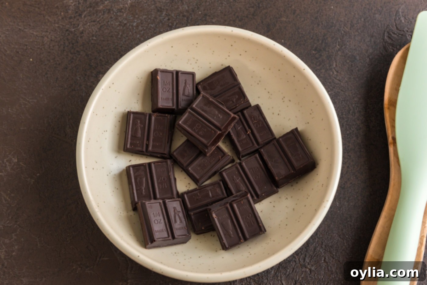 A selection of high-quality dark cocoa solid chocolate pieces arranged neatly on a white plate, ready for melting into the fudge frosting.