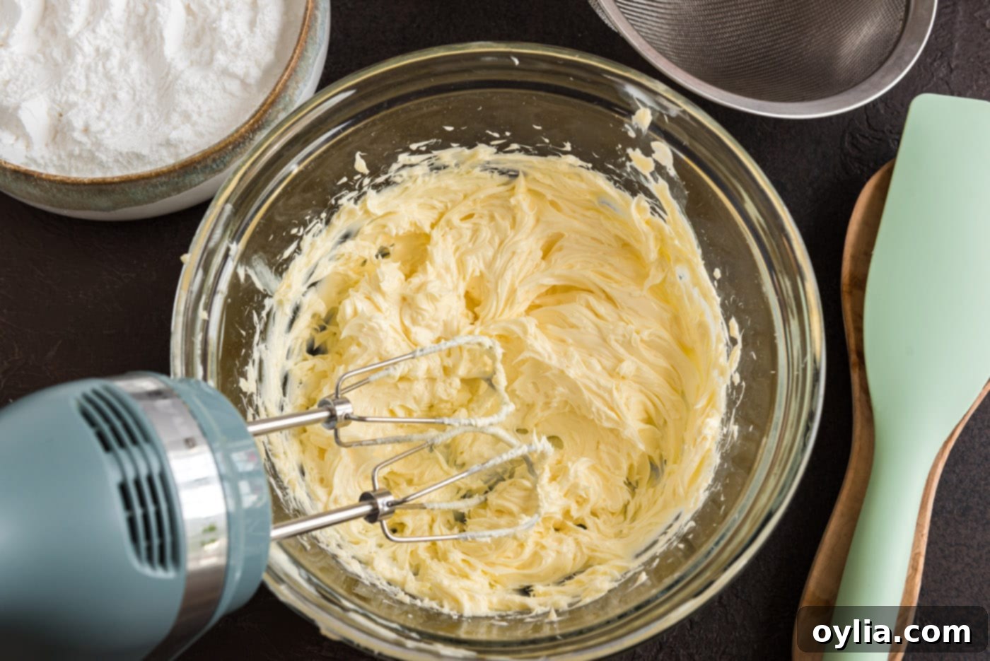 A hand mixer vigorously beats softened butter in a bowl, creating a light and creamy base for the fudge frosting.