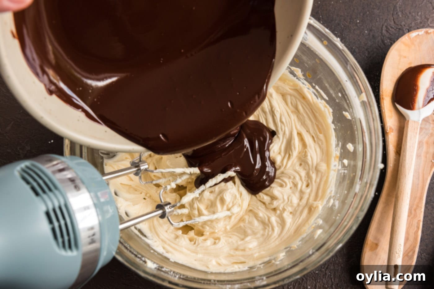 Melted dark chocolate is poured into the fluffy butter and powdered sugar mixture, ready to be blended into a rich chocolate fudge frosting.