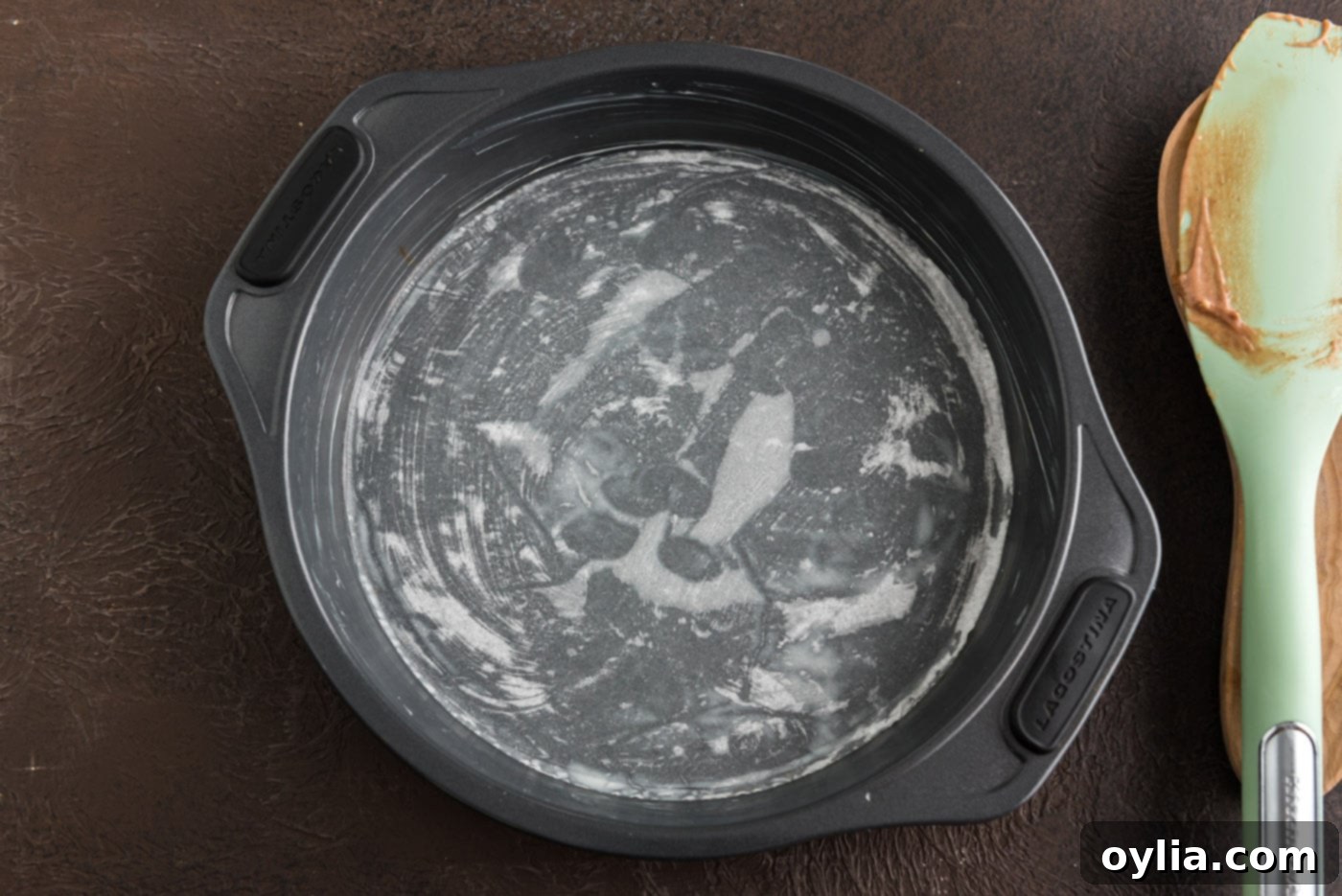 A greased 8-inch round cake pan lined with parchment paper at the bottom, ready for cake batter.
