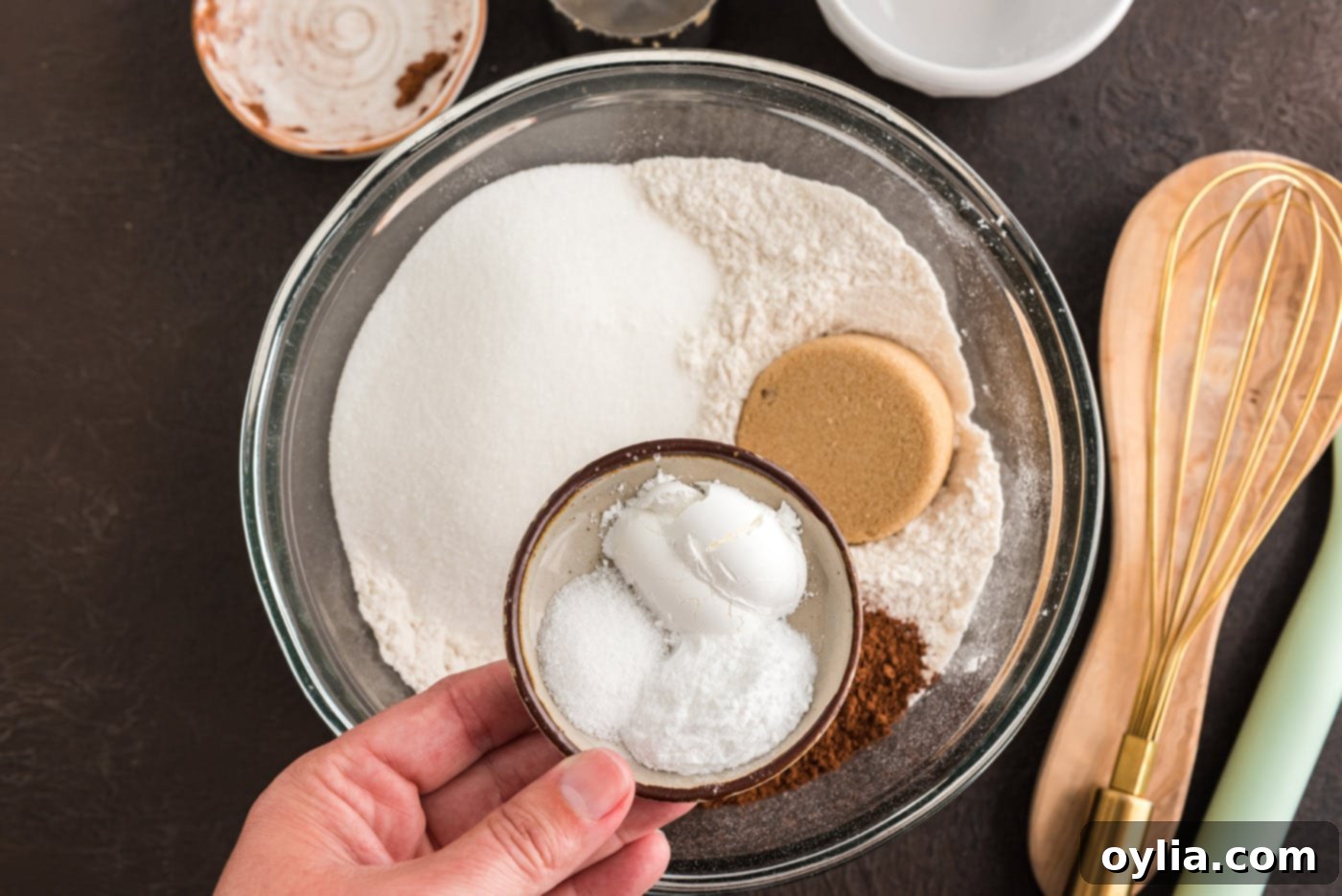 Various dry ingredients including flour, granulated sugar, cocoa powder, salt, baking powder, and baking soda are added into a large mixing bowl.