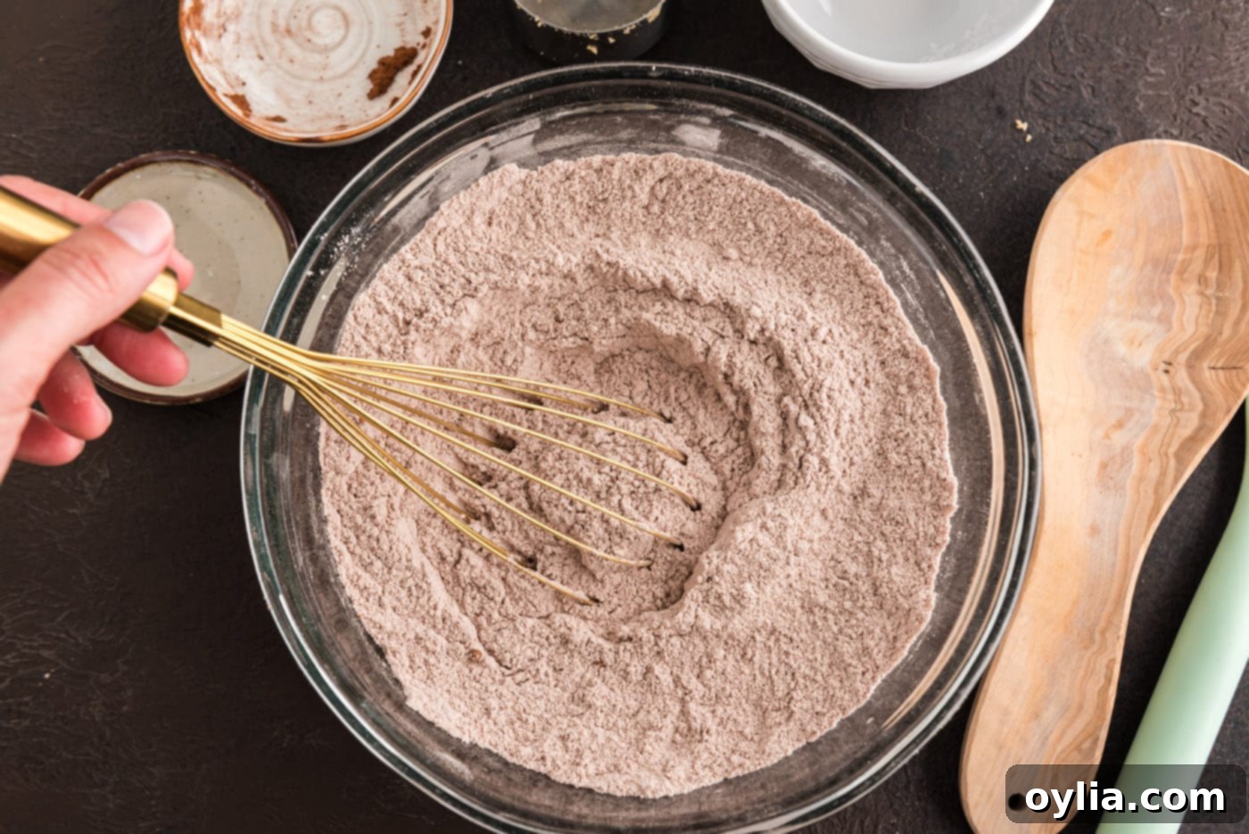 A whisk actively mixing the dry ingredients together in a large bowl, creating a uniform, pale brown mixture for the chocolate cake batter.
